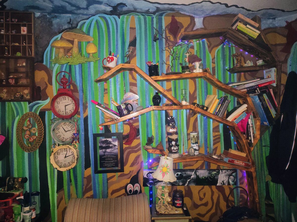 Handmade weeping willow tree bookshelf built into a mural wall, holding books, clocks, and curiosities